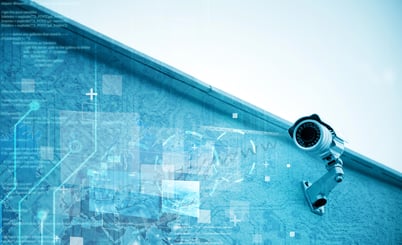 A security camera mounted on a building with a digital overlay featuring technology-themed graphics and code, symbolizing surveillance and data monitoring.